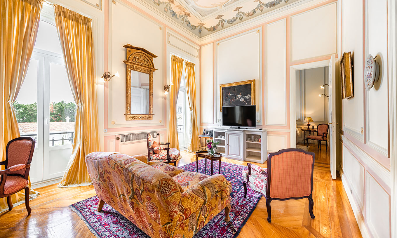 A Suite D. Amélia do Pestana Palace Lisboa tem uma sala de estar com sofá, cadeiras, televisão e duas janelas grandes