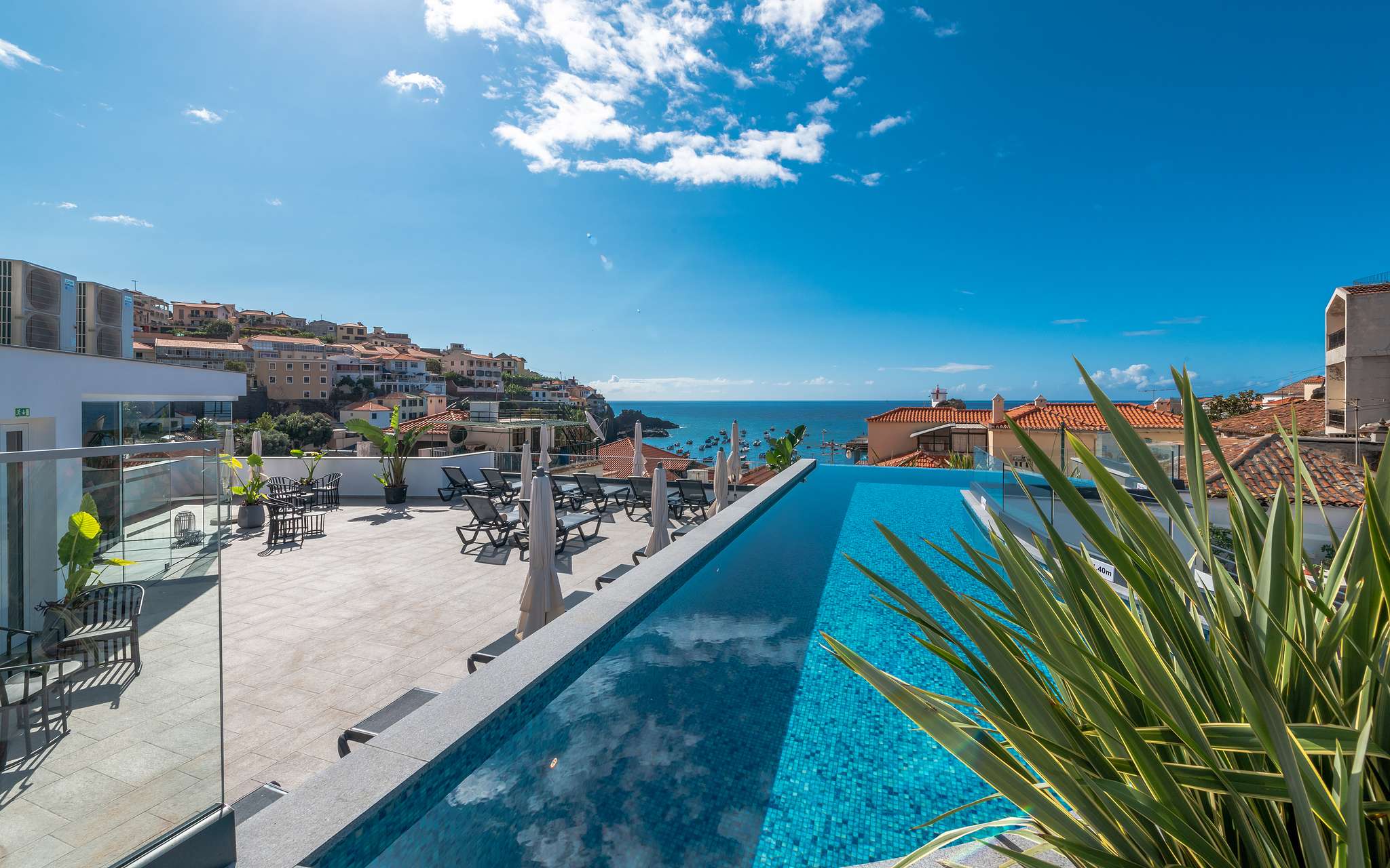 Vista da piscina exterior e esplanada do hotel em Câmara de Lobos, na Madeira, com o mar e cidade no fundo