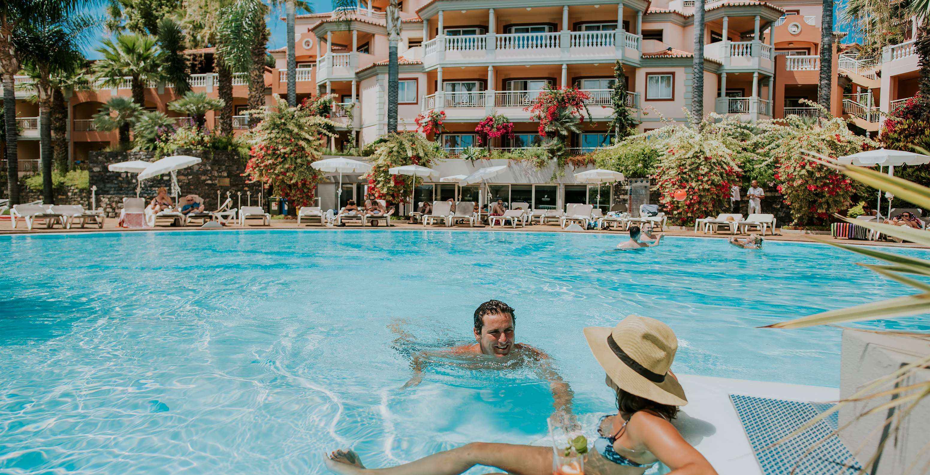 Casal na piscina, a conversar e a beber cocktails, no Pestana Miramar, um Hotel na Madeira Perto da Praia