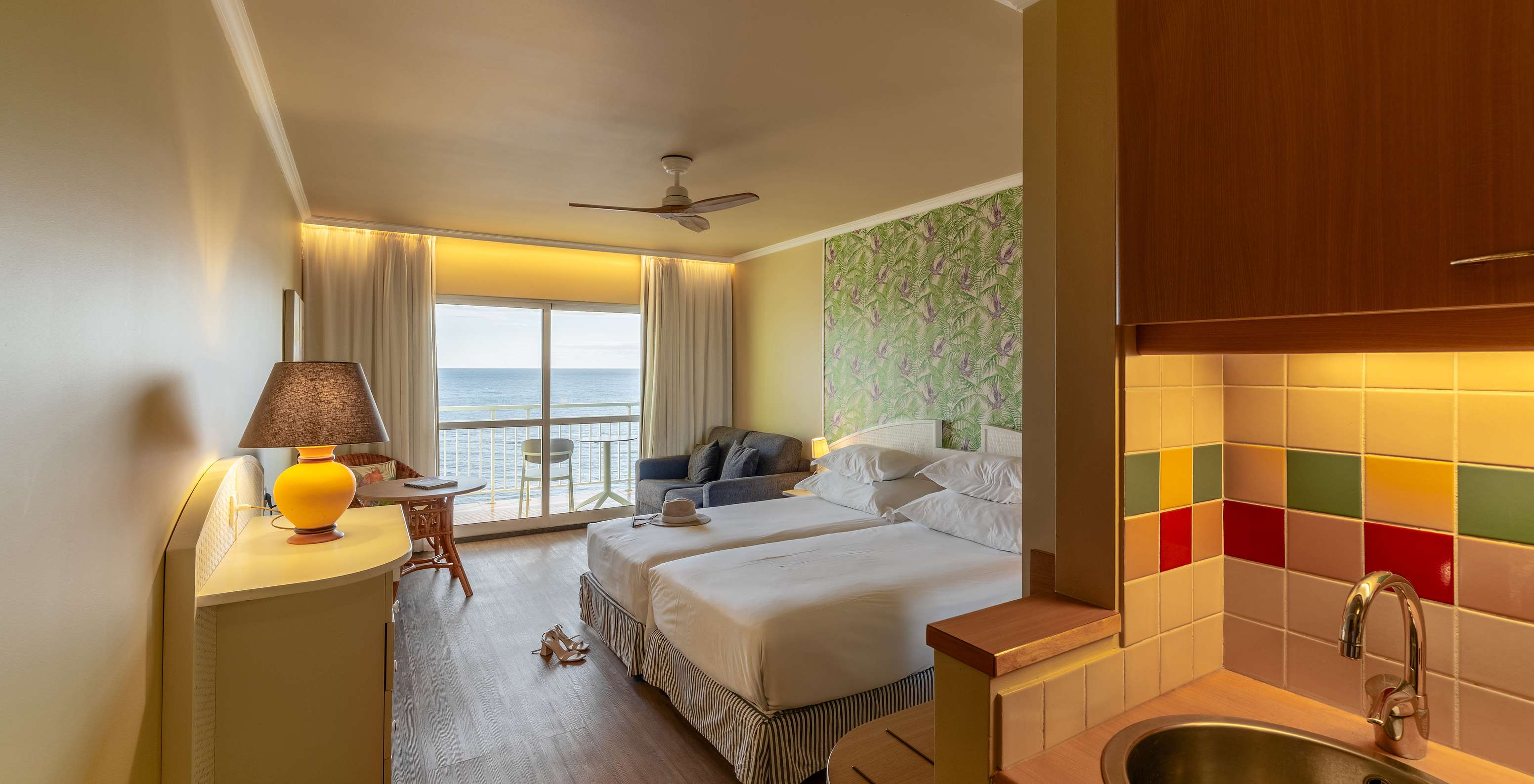 O Premium Sea View do Pestana Ocean Bay All Inclusive tem uma cama dupla, papel de parede com palmeiras, um sofá e varanda