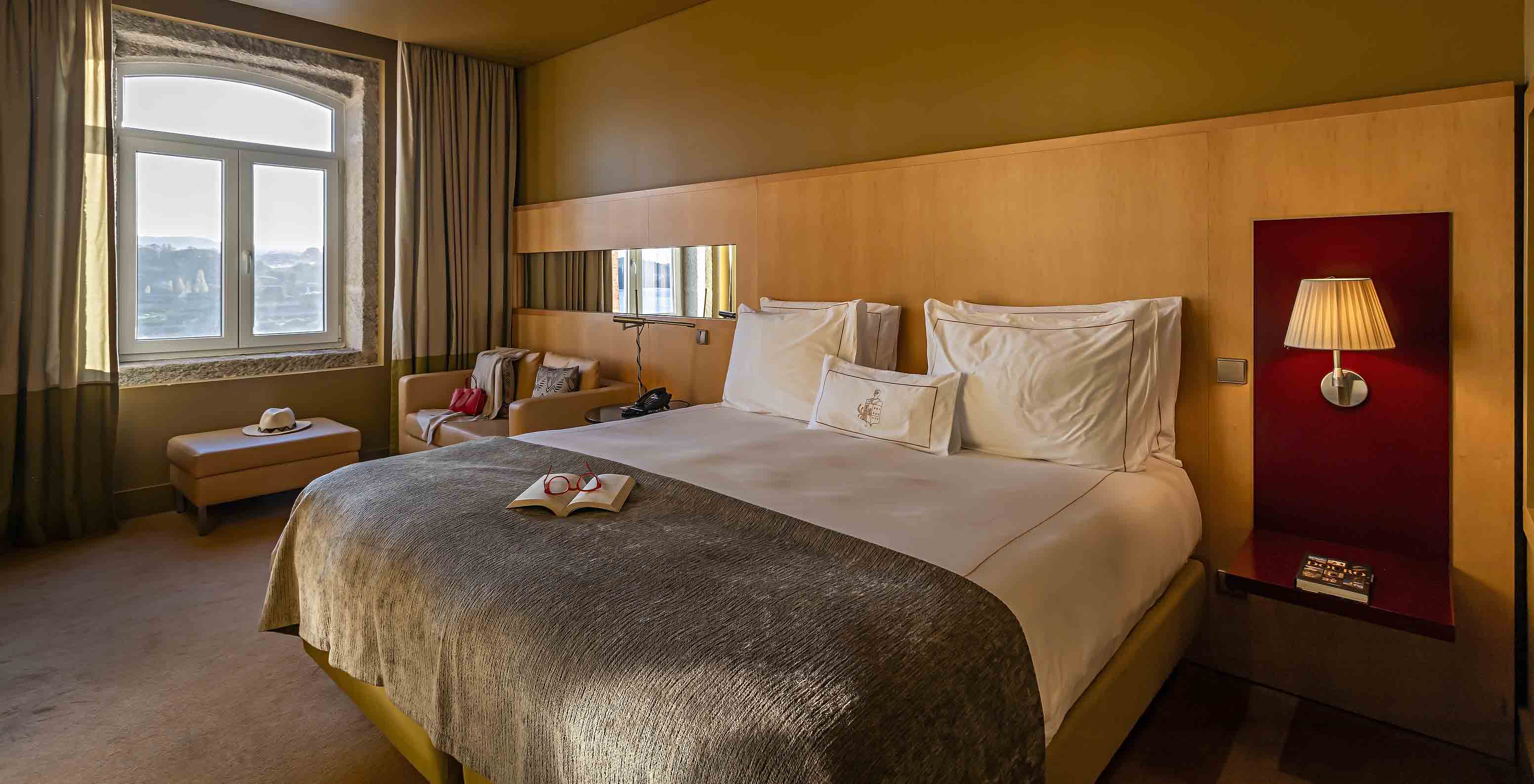 O Executive Superior do Pestana Palácio do Freixo tem uma cama de casal, um sofá e um puff ao lado da janela