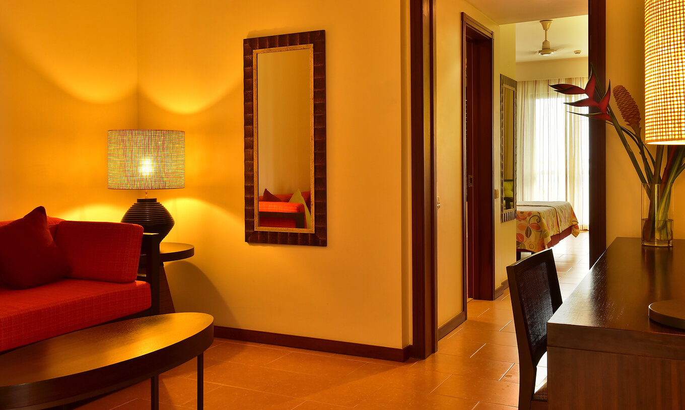 A Junior Suite do Pestana São Tomé tem uma sala com sofá vermelho e uma mesa de centro, e uma secretária com flores a decorar