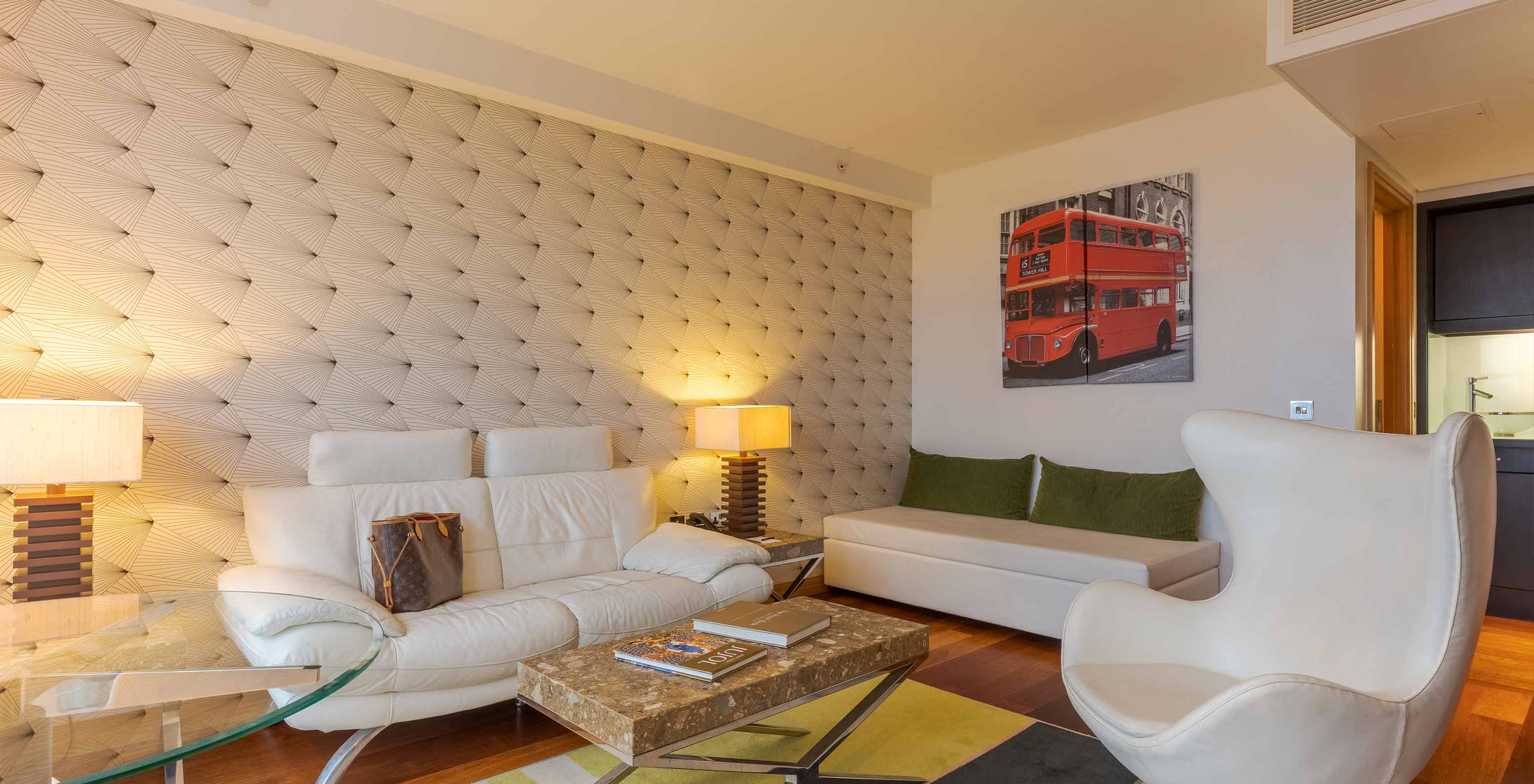 A Executive One Bedroom Suite do Pestana Chelsea Bridge tem um sofá e um pufe com mesa de centro, mesa de vidro e poltrona