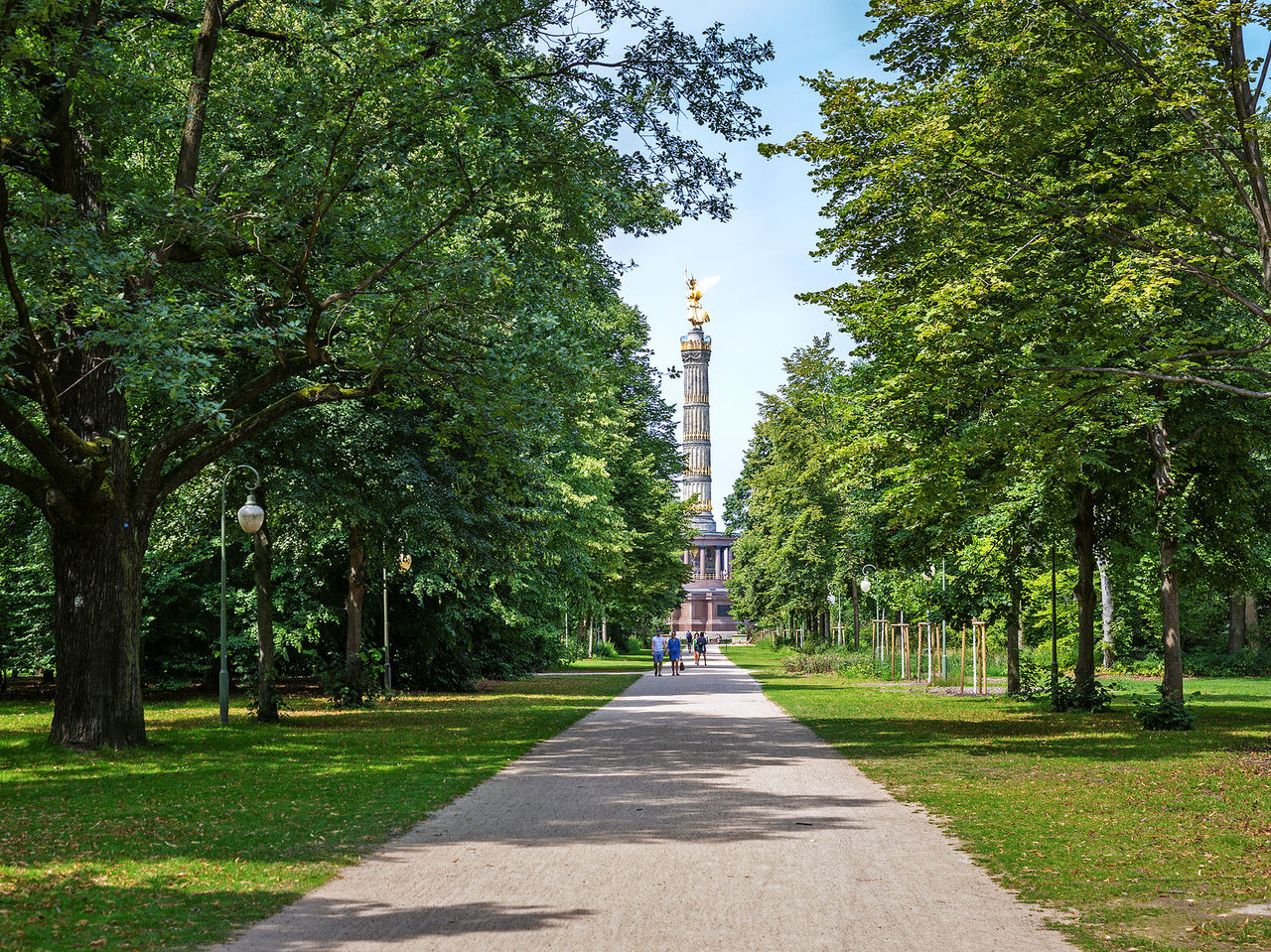 Park mit einem Weg, umgeben von Bäumen, in Berlin mit der berühmten Siegessäule im Hintergrund