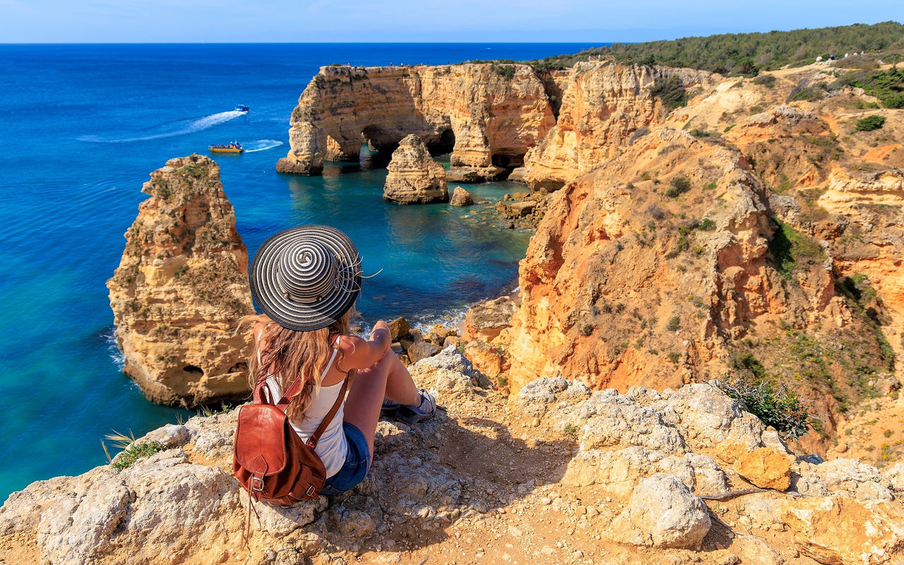 Frau bewundert den Panoramablick auf die Algarve-Küste, mit kristallklarem Wasser und einer von Vegetation umgebenen Klippe