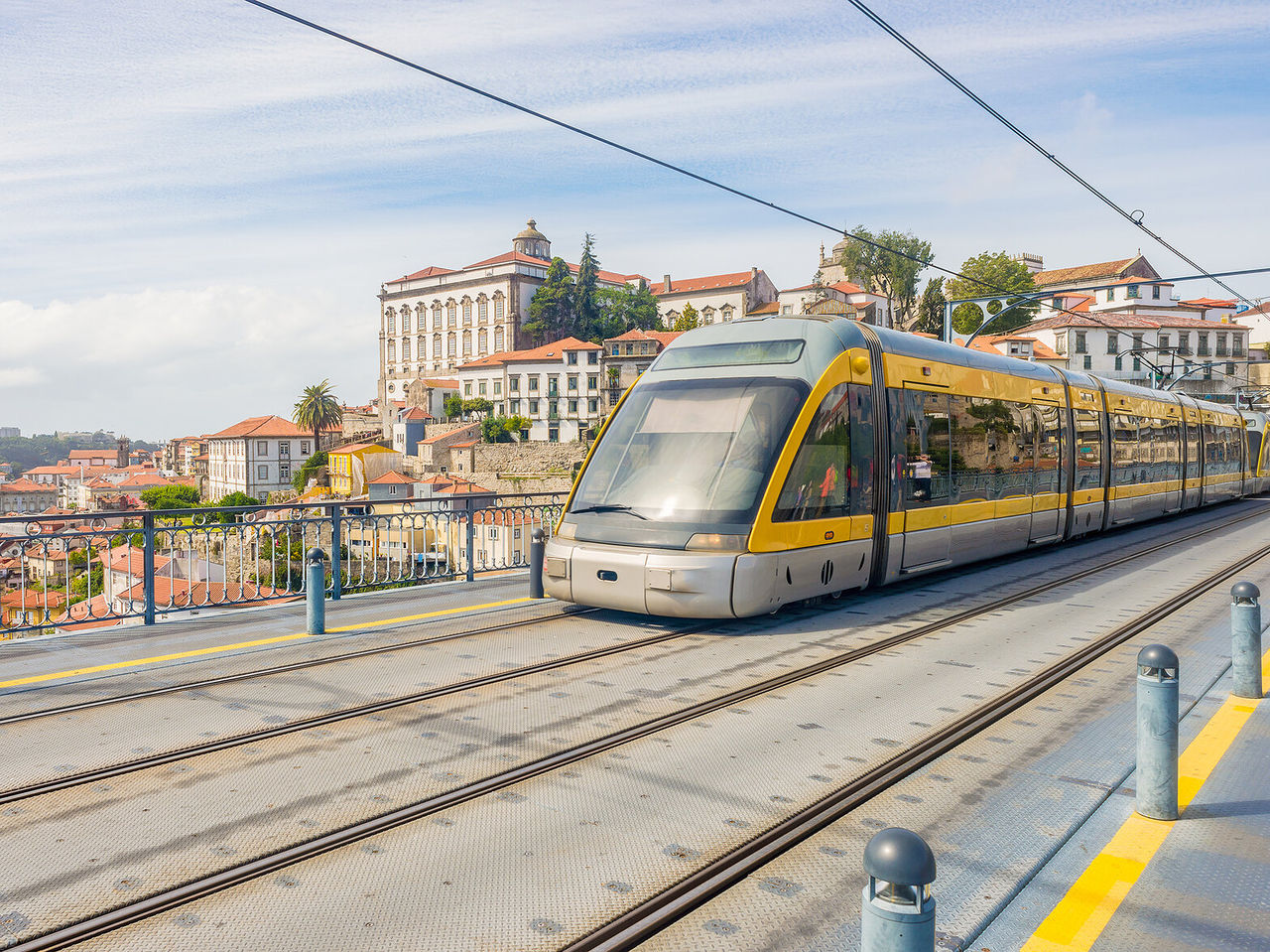 Blick auf eine moderne gelbe Straßenbahn mit der historischen Stadt Porto im Hintergrund, mit hohen und bunten Gebäuden