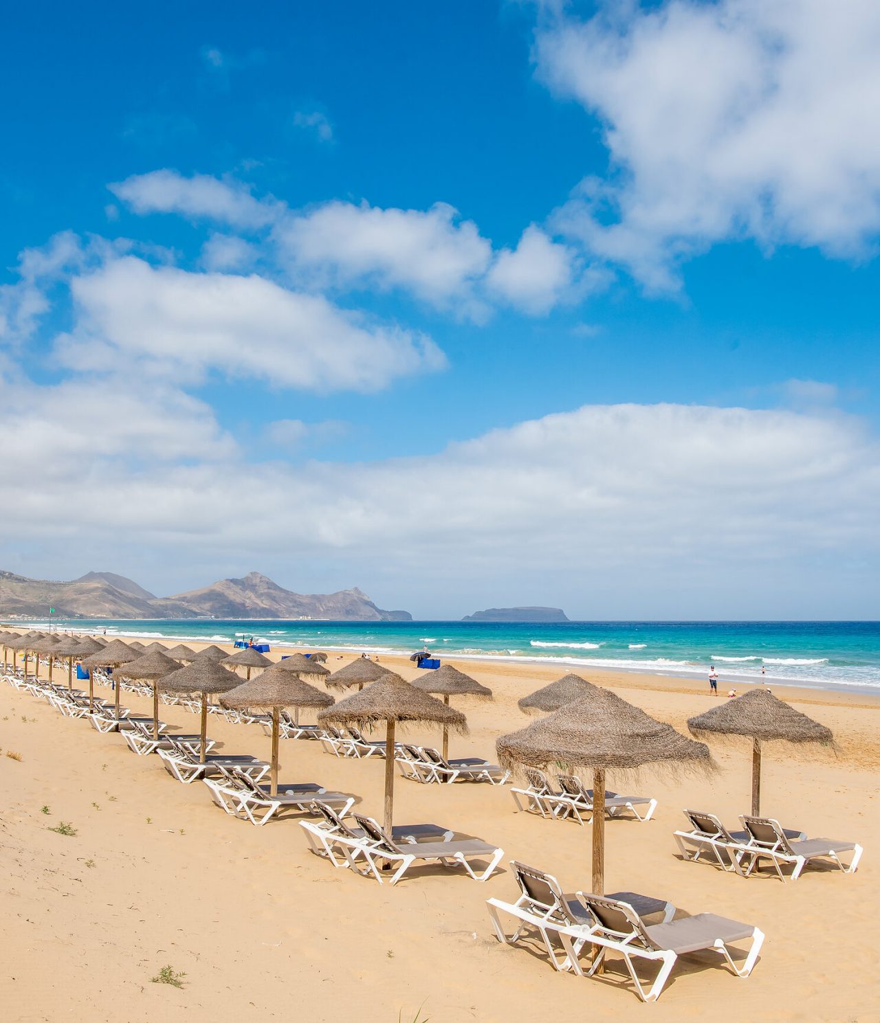 Strand von Porto Santo, mit mehreren Liegestühlen und Sonnenschirmen, türkisblauem Meer und goldenem Sand