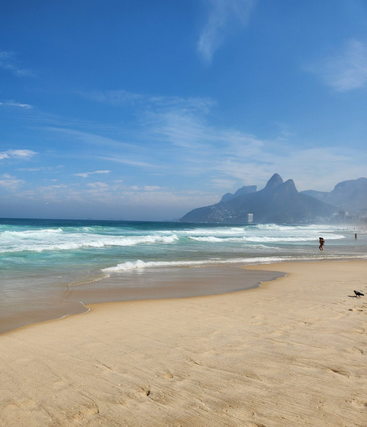 Blick auf einen Strand in Rio de Janeiro, mit weißem Sand, türkisfarbenem Wasser, Bergen und Menschen am Wasser