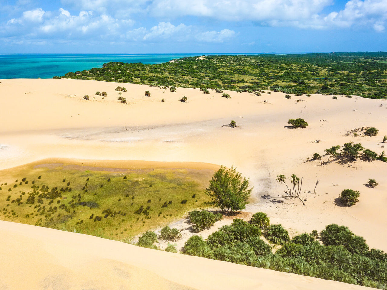 Aerial view of a desert landscape with white sand dunes contrasting with the crystal-clear ocean waters