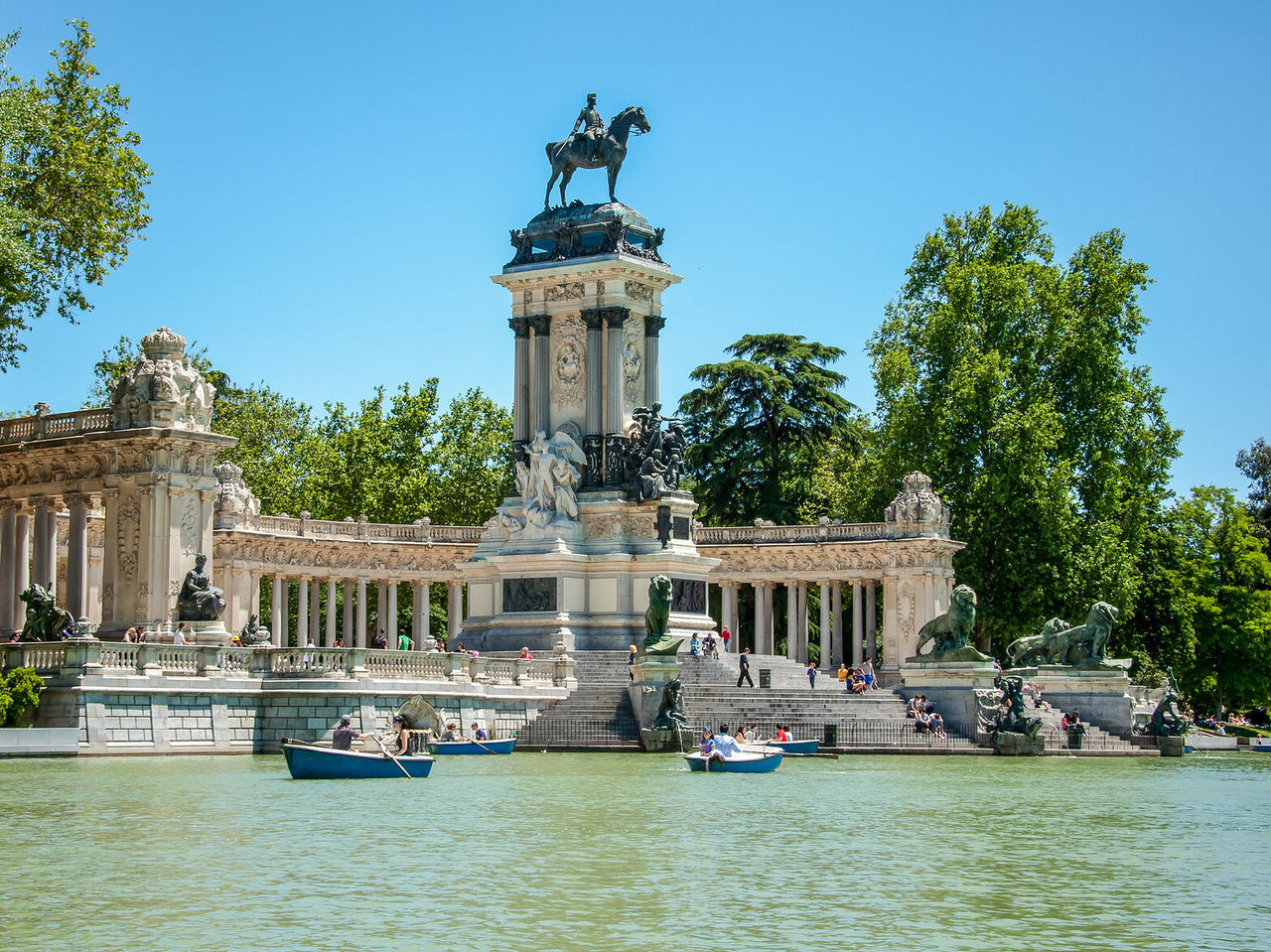 Lake at Retiro Park in central Madrid, with people rowing boats and others resting on the steps