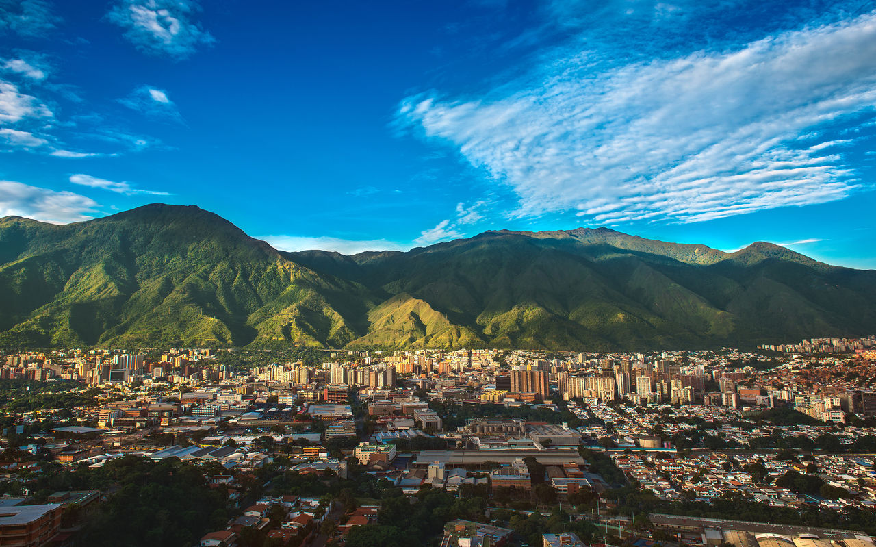Vista aérea de la ciudad de Caracas, con edificios altos, contrastando con la naturaleza montañosa y el cielo azul
