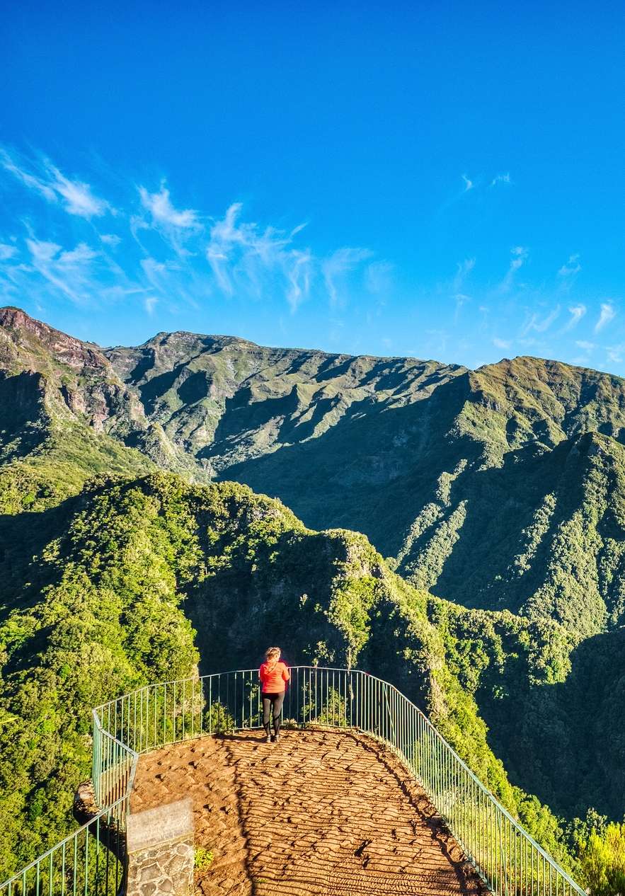 Persona caminando, parada para admirar el paisaje montañoso verde, en un mirador en Madeira