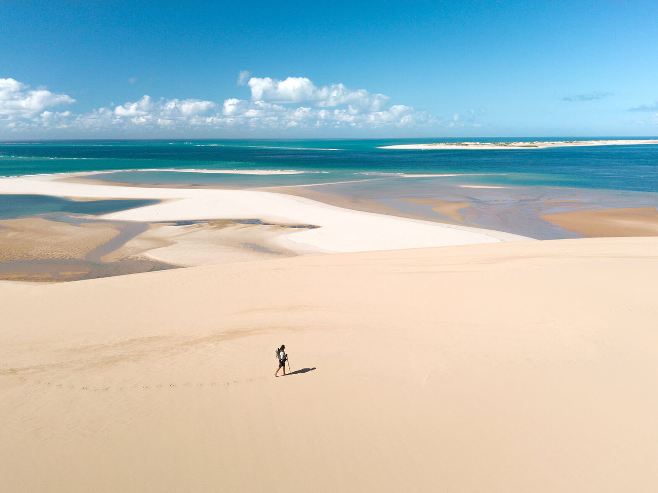 Un randonneur solitaire parcourant les vastes dunes de sable blanc de Bazaruto, avec l'océan Indien en arrière-plan