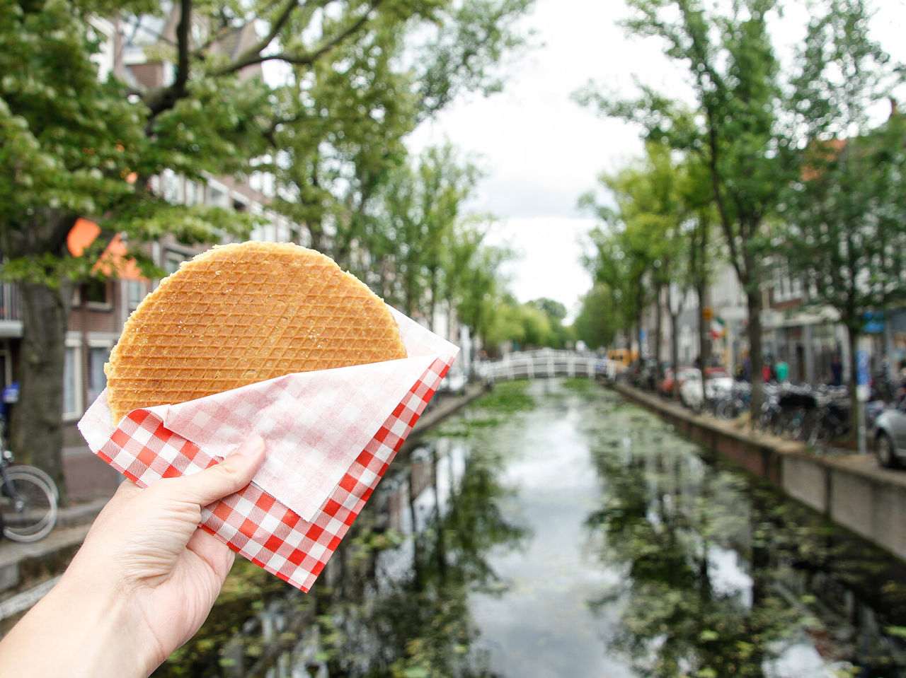 Main tenant un biscuit néerlandais, connu sous le nom de Stroopwafel, rempli de caramel, avec un canal en arrière-plan