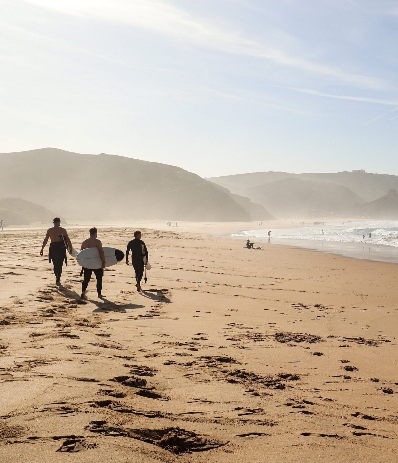 Surfeurs portant leur planche de surf sur une plage de la côte de l'Algarve, avec des vagues et des rochers en arrière-plan