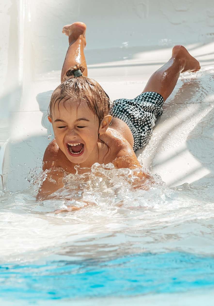 Enfant souriant glissant sur le toboggan du parc Slide & Splash vers la piscine