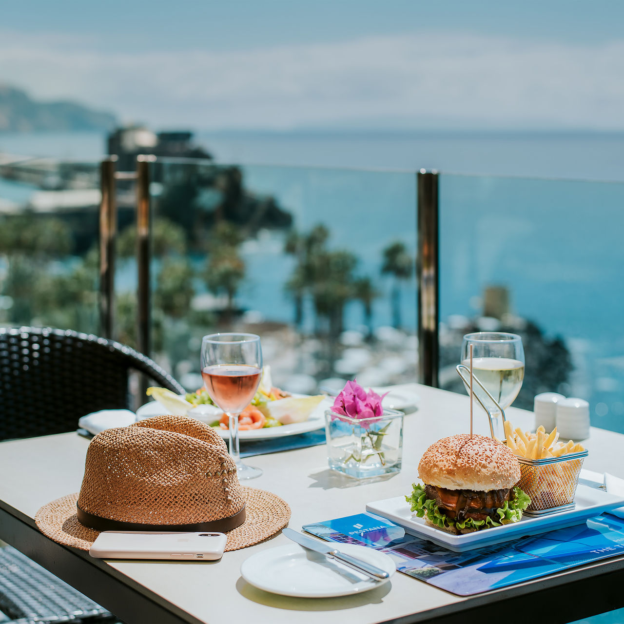 Table du Pestana Madeira Beach Club avec vue sur la mer, hamburgers, frites, vin et un chapeau