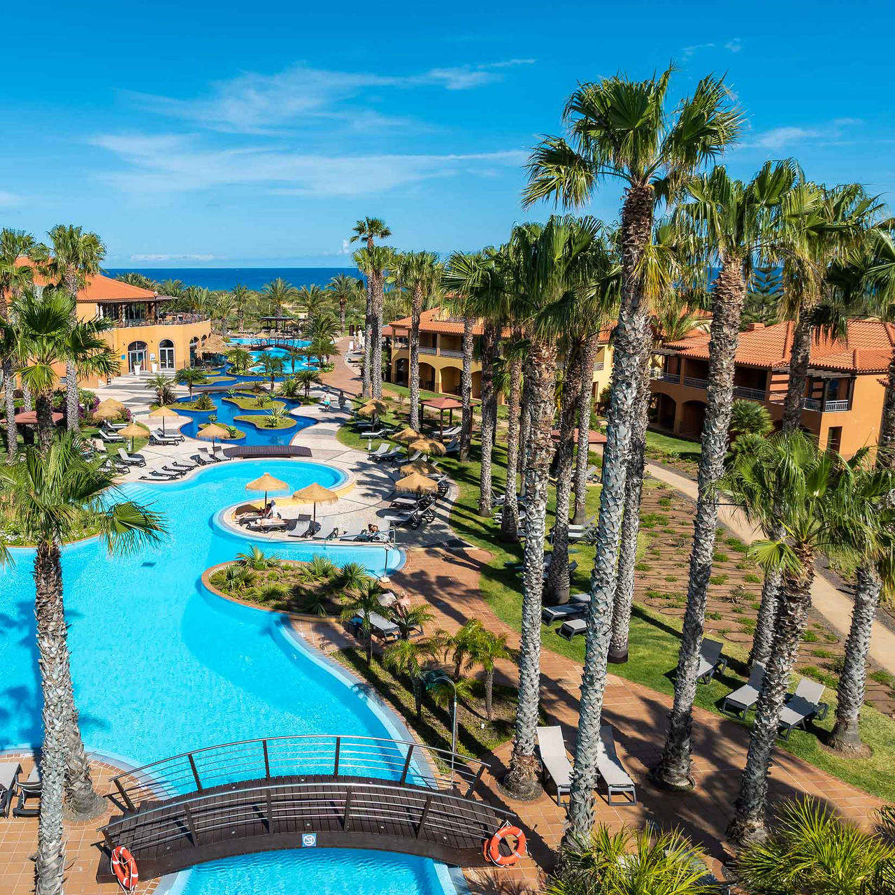 Piscine du complexe hôtelier 5 étoiles à Porto Santo, entourée de palmiers tropicaux, de chaises longues et de jardin.