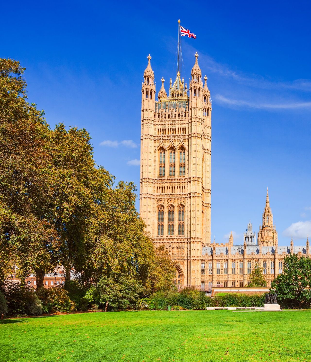 Vue d'un jardin avec un palais, avec une architecture typique de Londres, des arbres devant et un drapeau au sommet