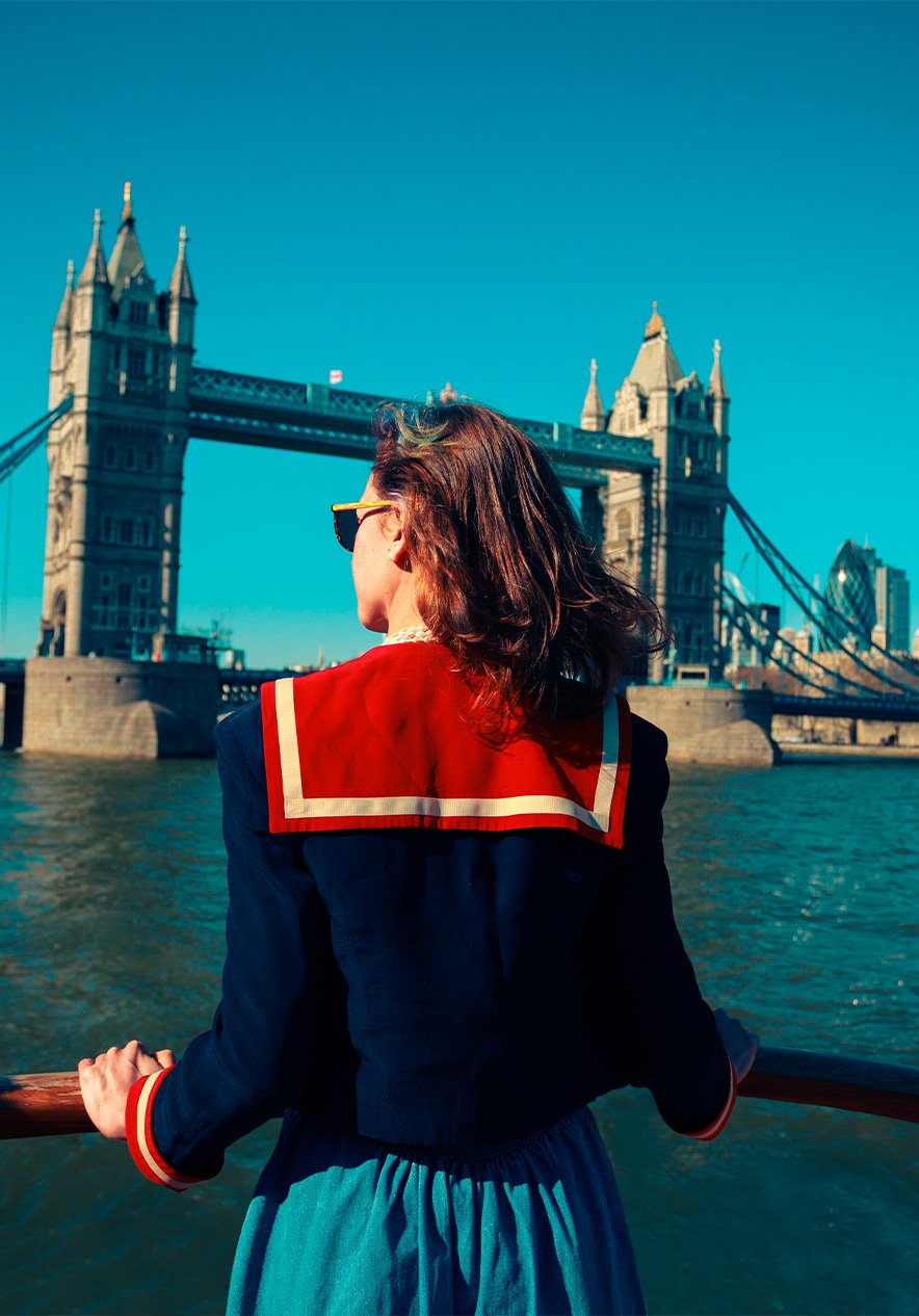 Promenade en bateau sur la Tamise avec une dame à l'avant du bateau, tournée vers Tower Bridge, sous un ciel dégagé