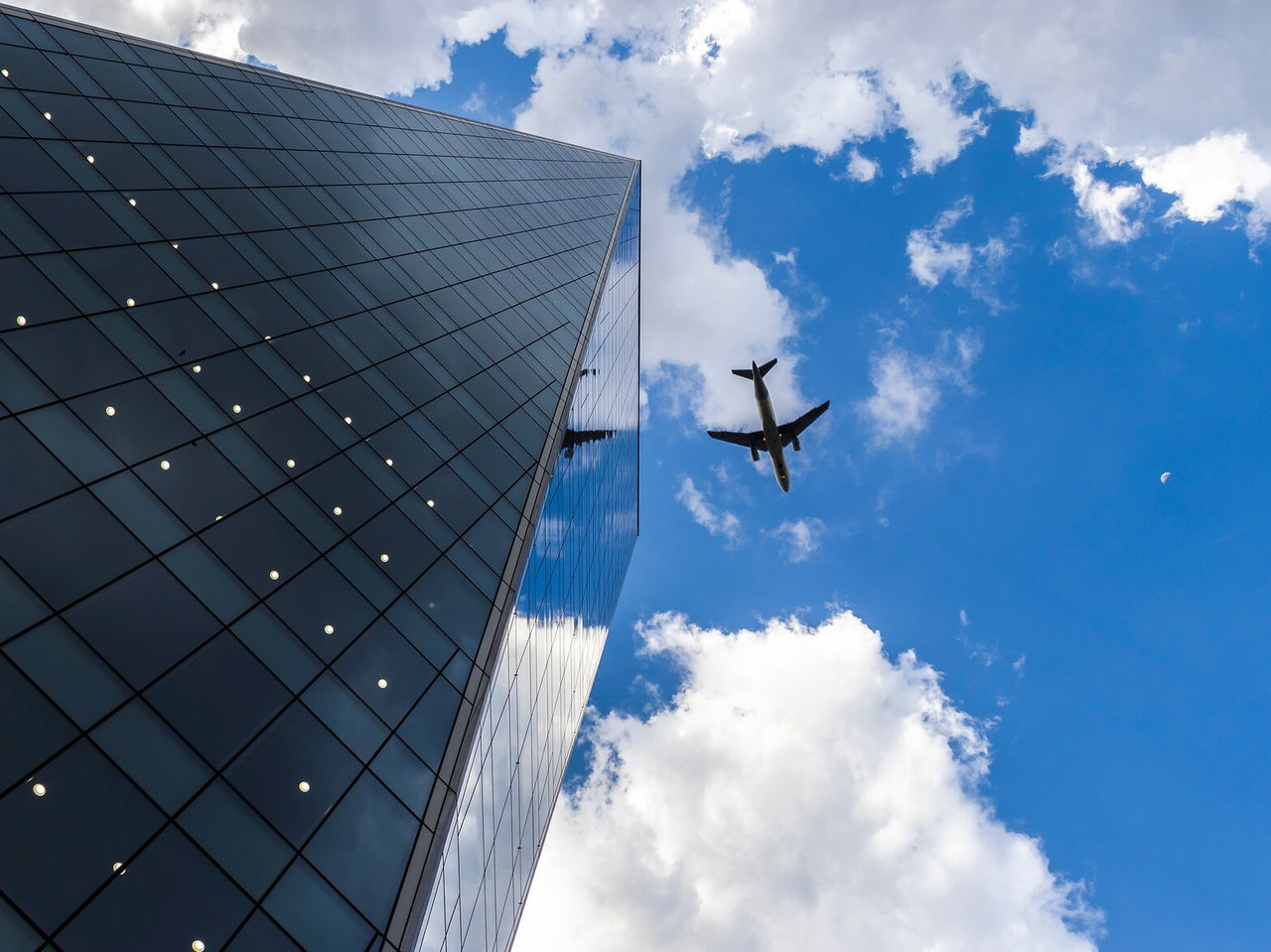 Façade en verre d'un bâtiment à São Paulo avec des reflets de nuages et un avion en vol