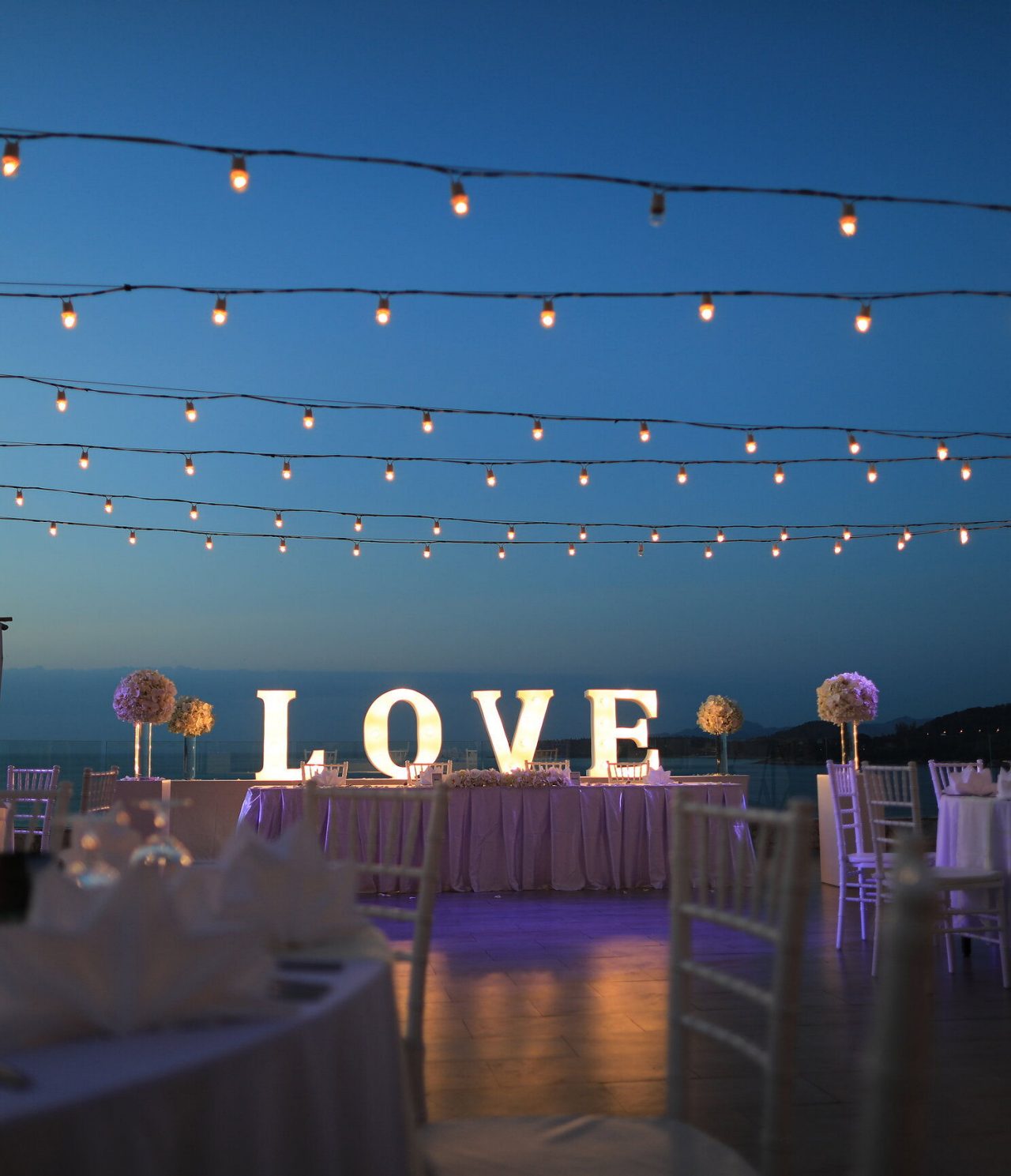 Décoration pour votre occasion spéciale, avec des tables extérieures, des lumières suspendues et une grande pancarte "Love"