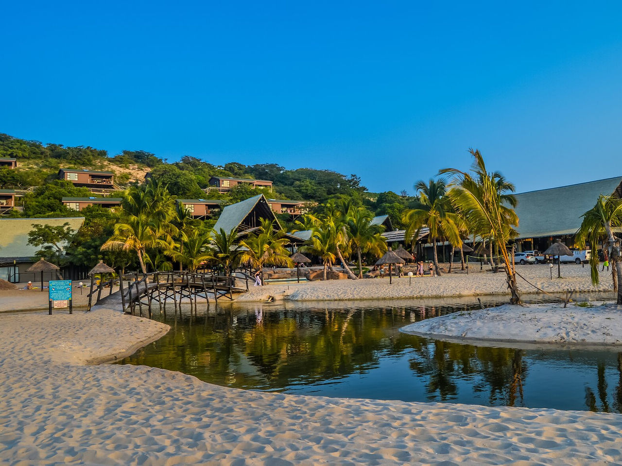 Strand in Maputo met een rivier door het zand, brug om over te steken, verspreide palmbomen