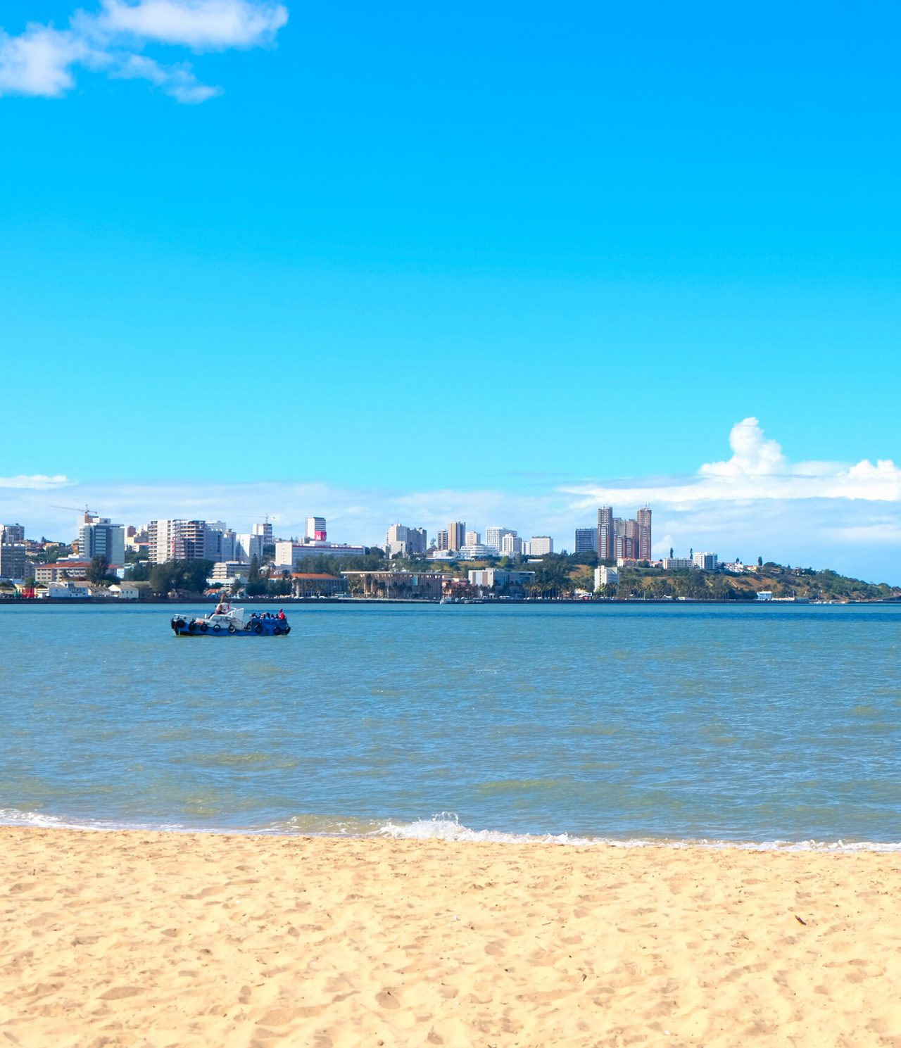 Uitzicht op de stad Maputo van de overkant van de rivier, op een strand waar meerdere kinderen met het water spelen