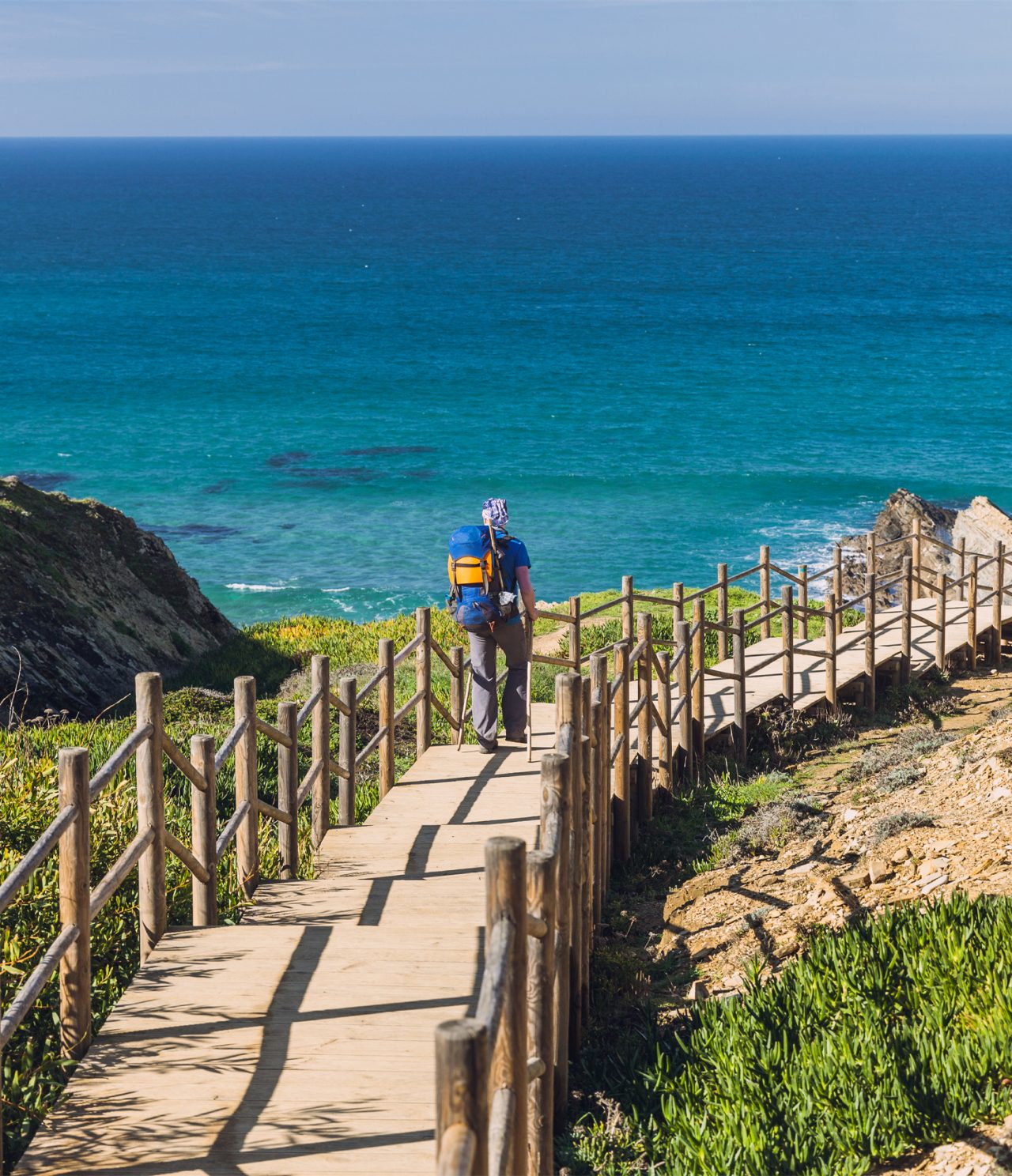 Man loopt over een houten wandelpad naar een strand in Alentejo, met kristalhelder water