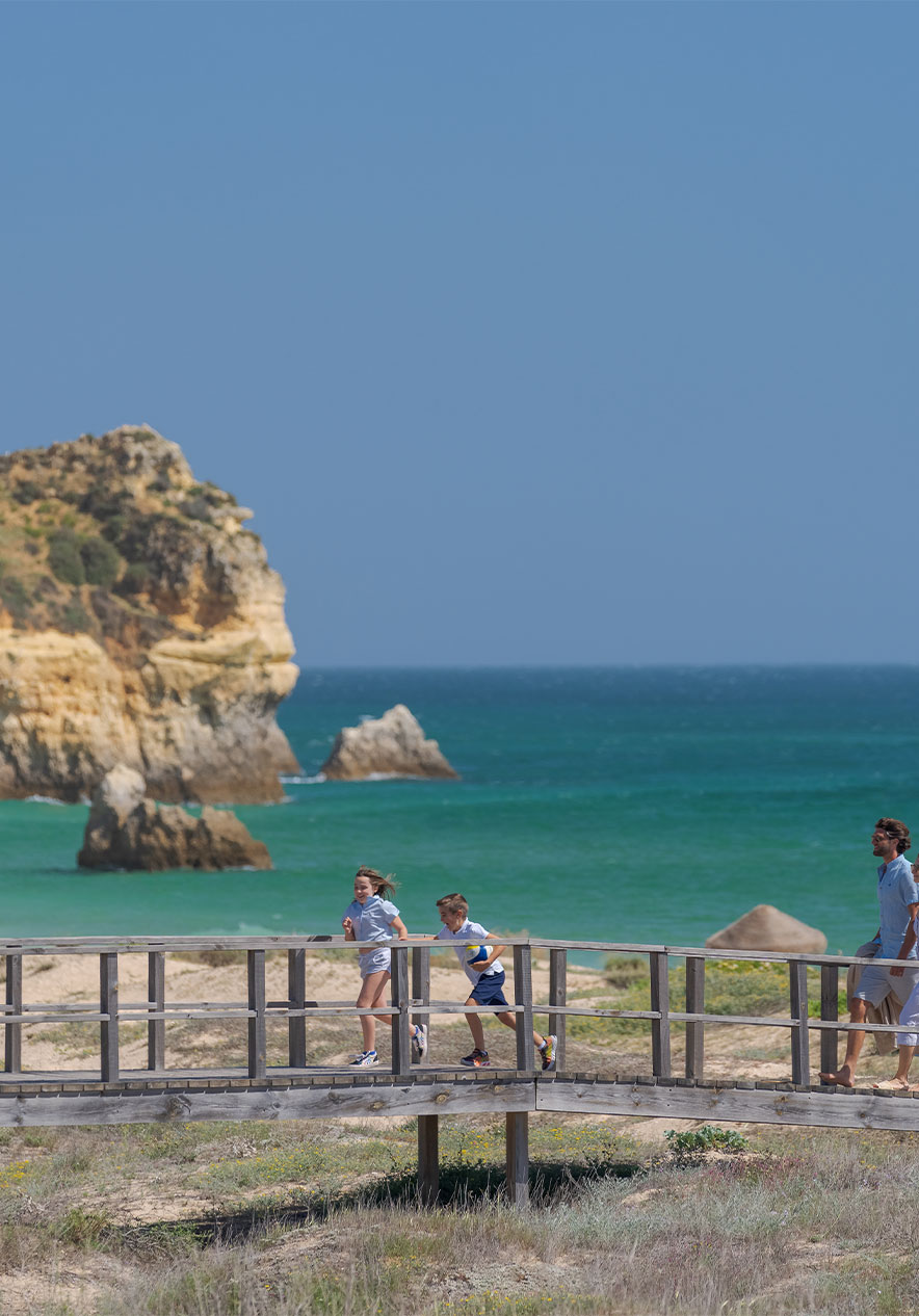 Kinderen rennen lachend over de loopbrug van Praia do Alvor, met helderblauw water en gouden zand