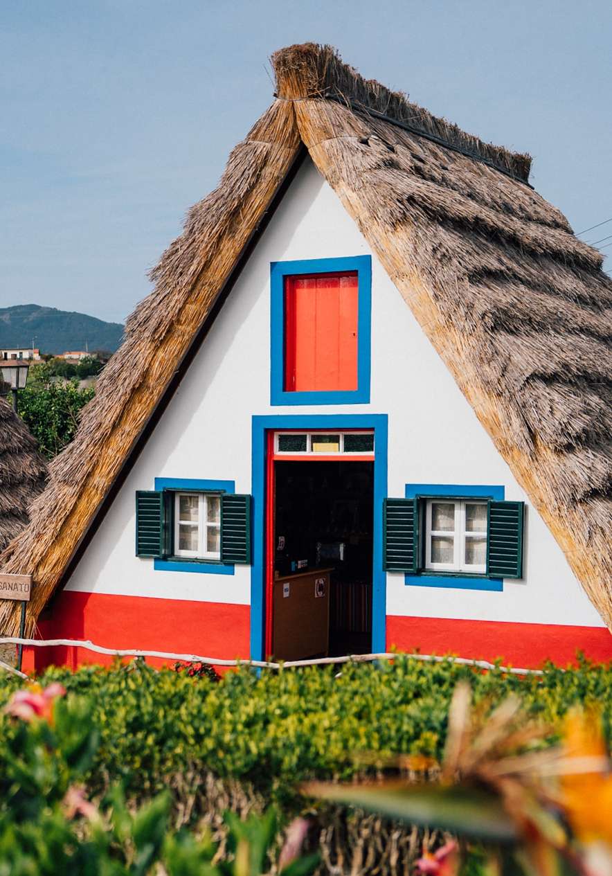 Twee traditionele huizen met rieten daken, geschilderd in wit met rode en blauwe details in Funchal