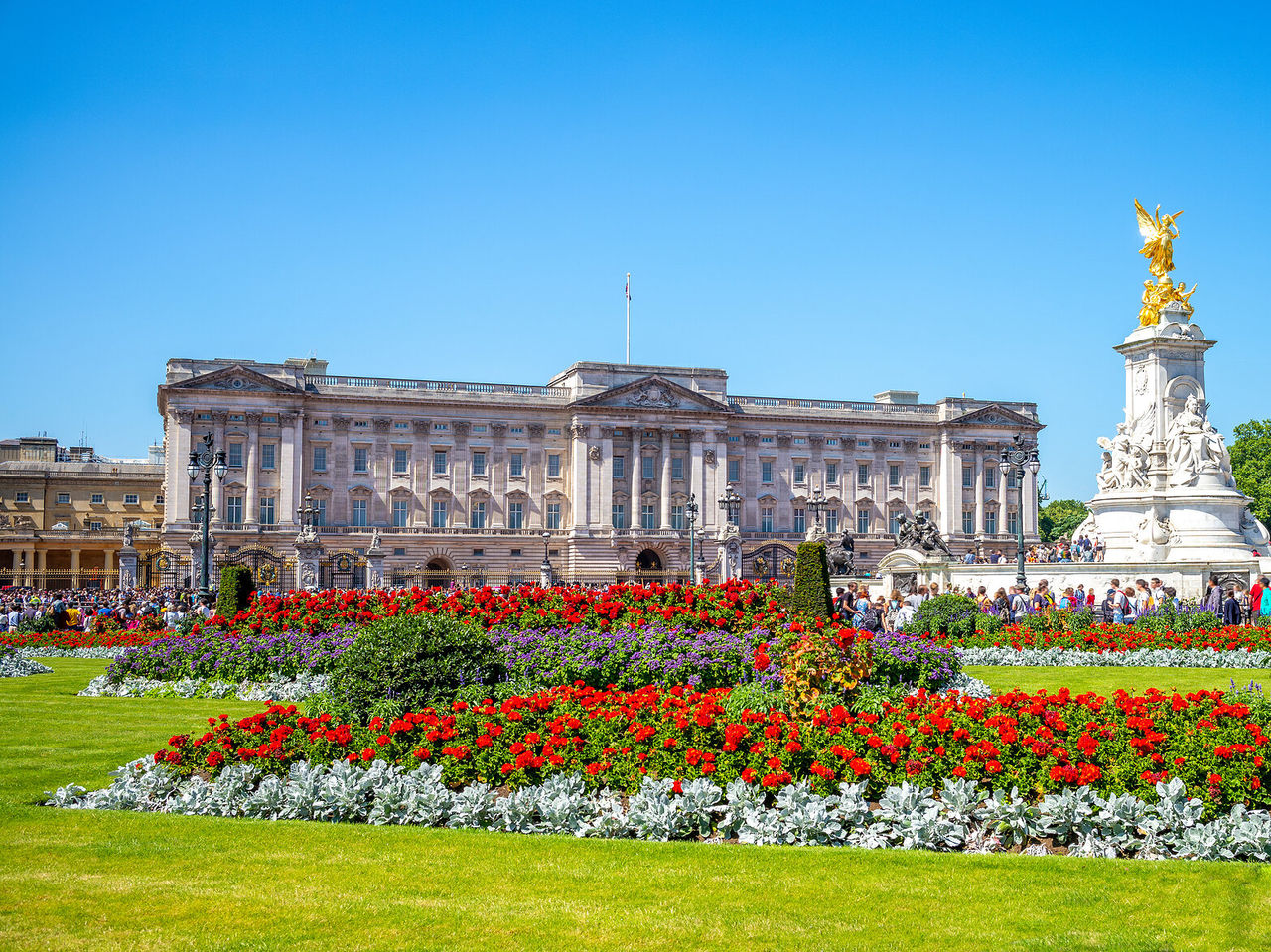 De imposante gevel van Buckingham Palace in Londen, met een gouden standbeeld en een bloementuin ervoor