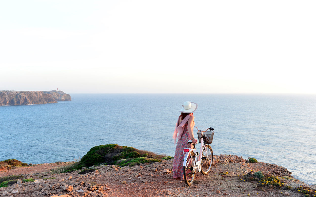 Vrouw loopt met een fiets in de hand langs de kliffen aan de Portugese kust, aangeboden door Pousadas de Portugal