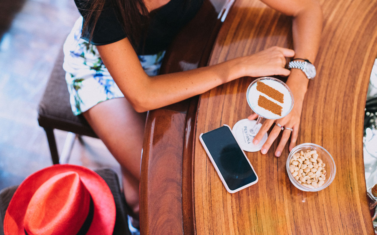 Rapariga sentada no Bar do Hotel, toma um cocktail com um logotipo em canela do Pestana Hotel Group