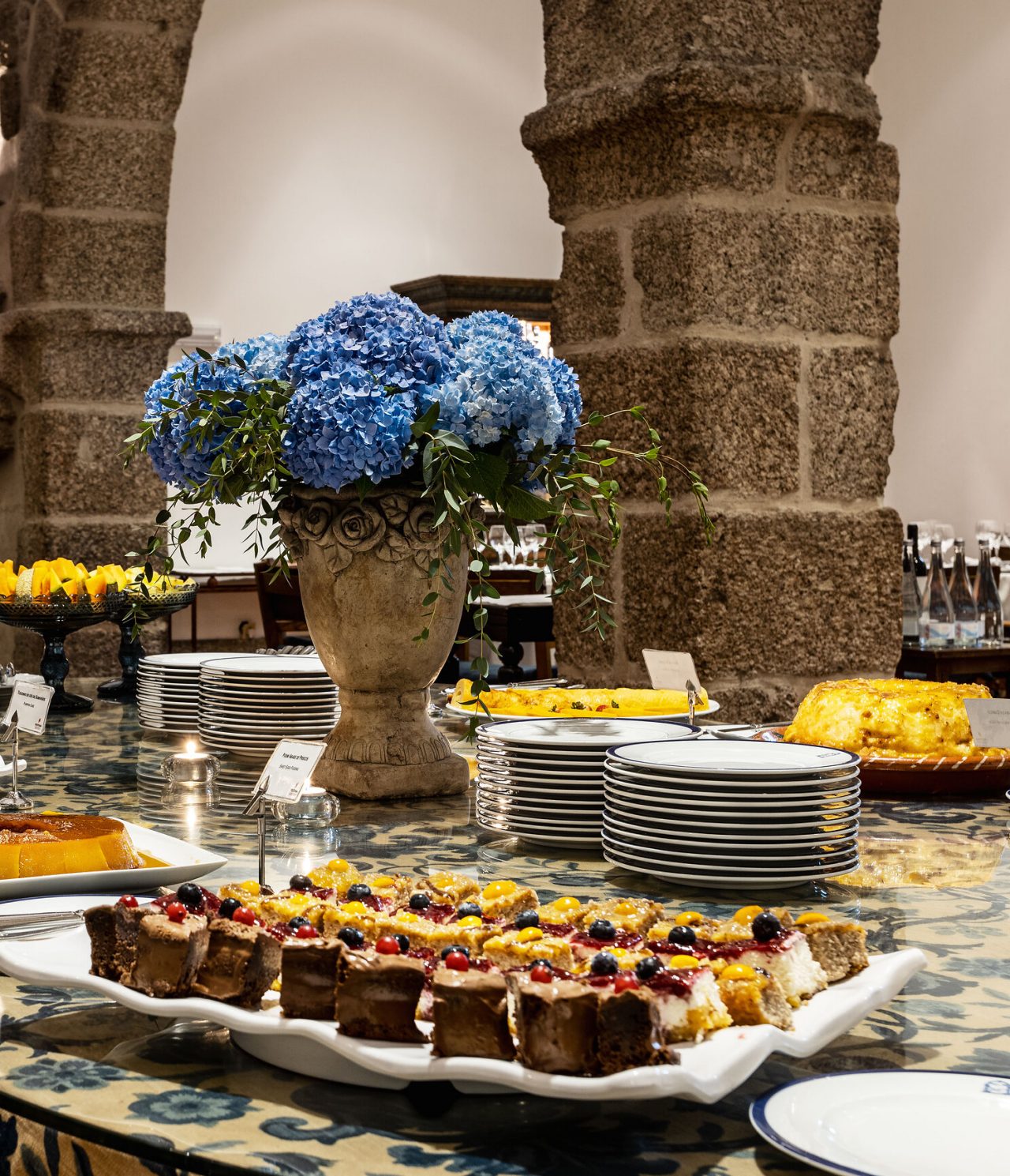 Mesa decorada com uma variedade de doces, desde bolos e tortas até frutas frescas numa sala com móveis antigos 