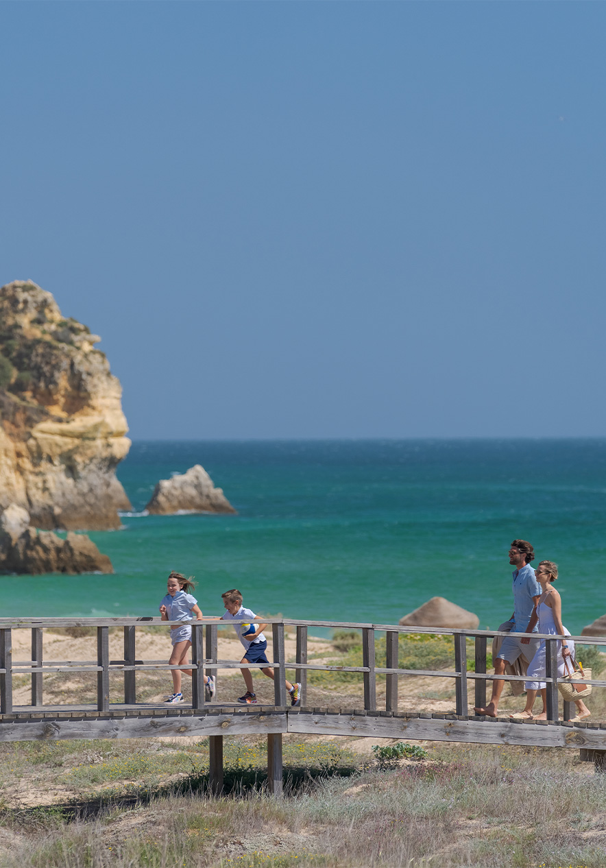 Wooden boardwalks of Alvor beaches with the sea in the background and two children running with their parents behind