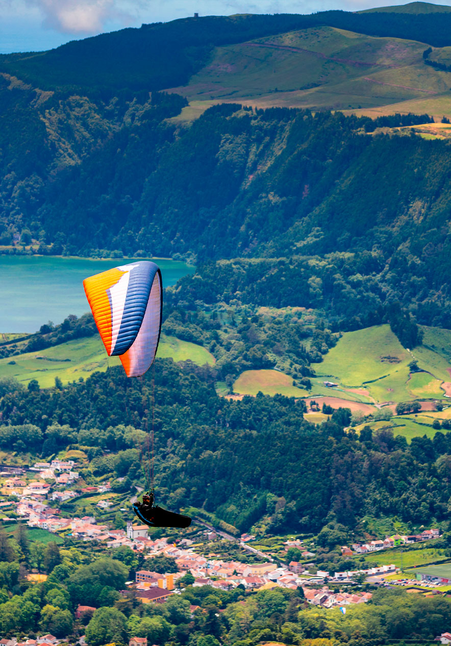 Man paragliding in São Miguel Island over land with houses and green mountainous fields