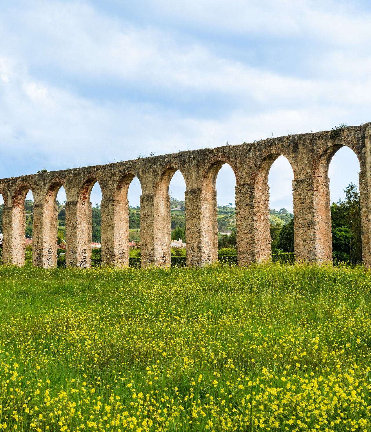 Imposing stone aqueduct with high arches contrasting with a yellow flowered field