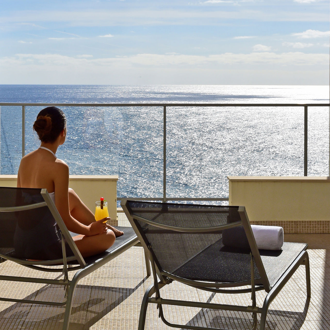 Woman sitting on a lounger drinking a cocktail on the balcony of a 4-star hotel by the sea in Funchal