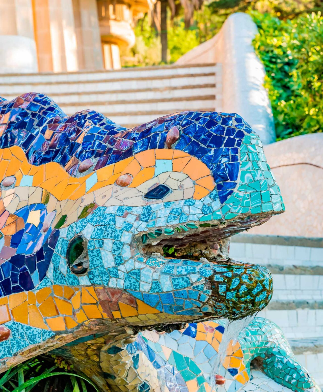 The iconic colorful dragon sculpture, a work by Gaudí, in Park Güell, Barcelona, with stairs and vegetation in the background