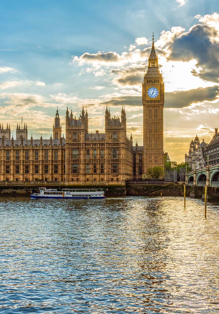 View of Big Ben and Buckingham Palace with sunlight peeking through the clouds with the river and bridge on the side